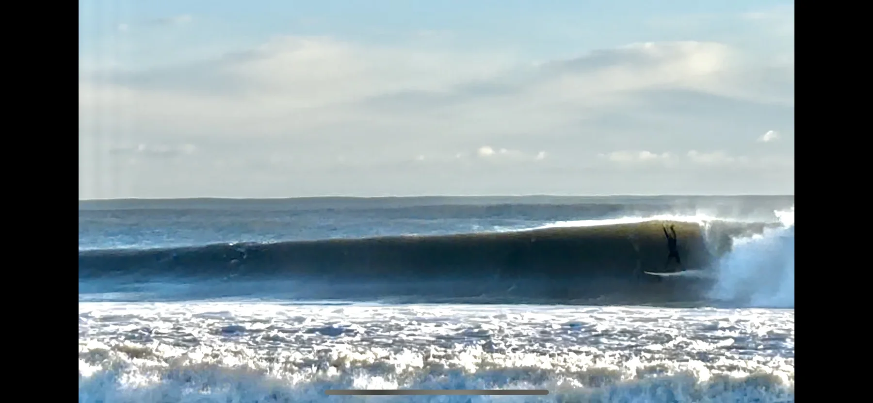 A surfer riding a clean wave under an open sky